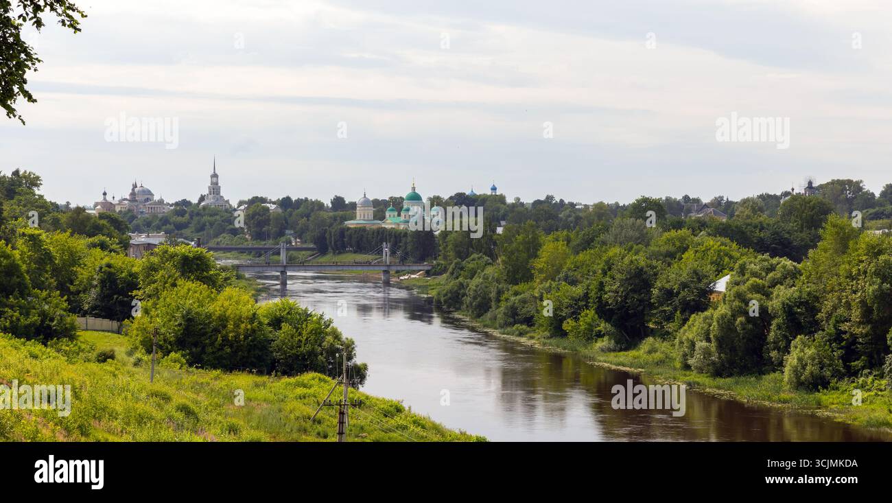 Vue panoramique sur la rivière tranquille avec une végétation luxuriante et une ligne d'horizon de la ville présentant l'architecture historique, créant une ambiance sereine. Torzhok, Russie Banque D'Images
