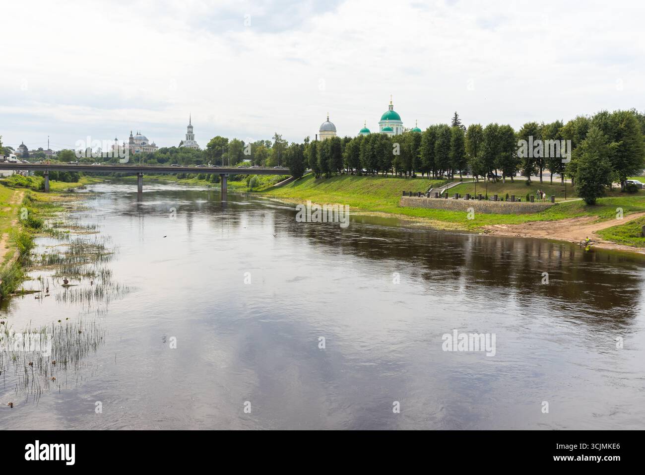 Torzhok, Russie. Scène fluviale tranquille avec une végétation luxuriante et une ligne d'horizon de la ville présentant l'architecture historique, créant une ambiance sereine Banque D'Images