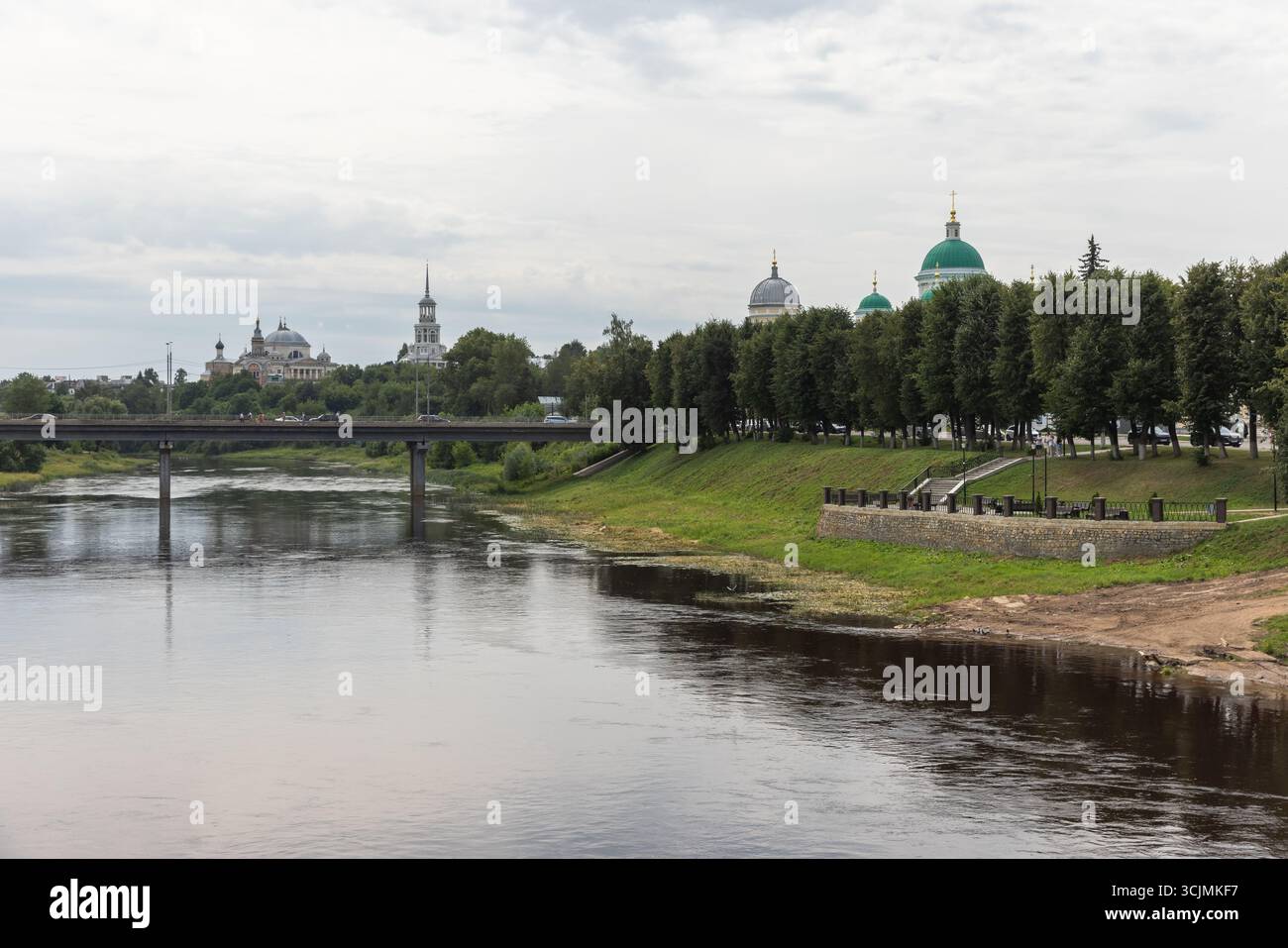 Paysage urbain de la vieille ville de Torzhok avec une rivière tranquille enjambée par un pont, une végétation luxuriante et des dômes architecturaux historiques en arrière-plan. RU Banque D'Images