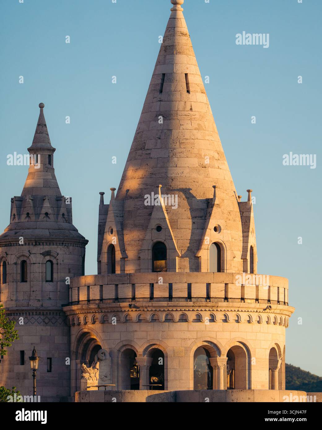 Vue sur les tours de pierre ornées du Bastion des pêcheurs s'élèvent majestueusement contre un ciel bleu clair, leurs toits coniques et leurs fenêtres cintrées projetant des ombres dans la lumière chaude du soleil, Budapest, Hongrie. Banque D'Images