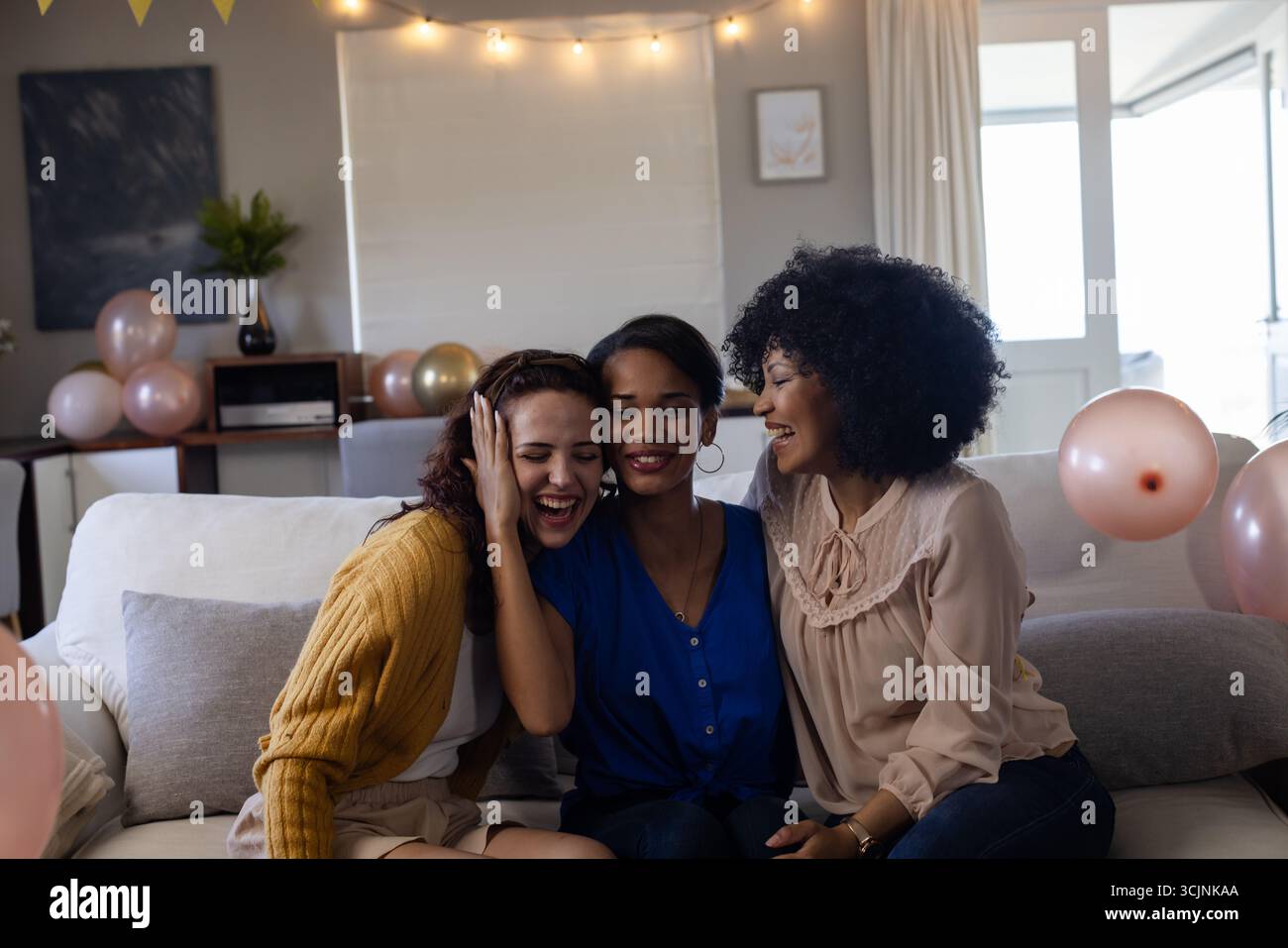 Trois femmes assises sur le canapé riant et célébrant à la maison avec des ballons Banque D'Images