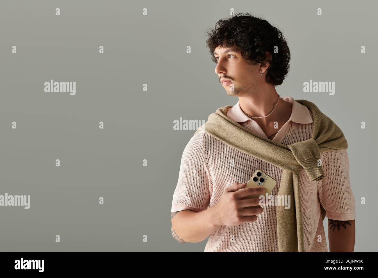 Jeune homme respire la confiance à travers la mode, posant sur une toile de fond simple avec un téléphone. Banque D'Images