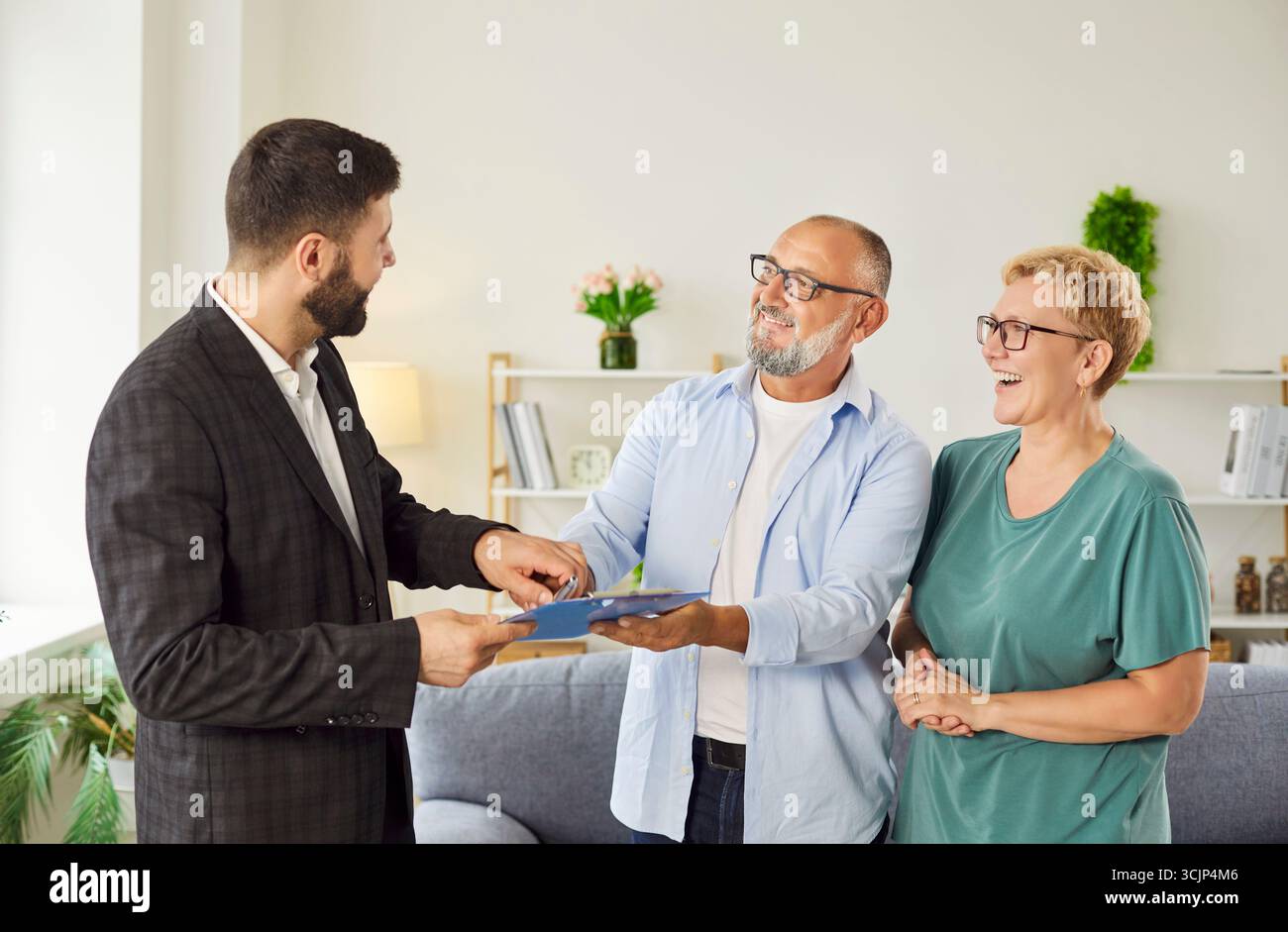 Agent immobilier présentant le contrat à un couple souriant dans le salon de la maison Banque D'Images