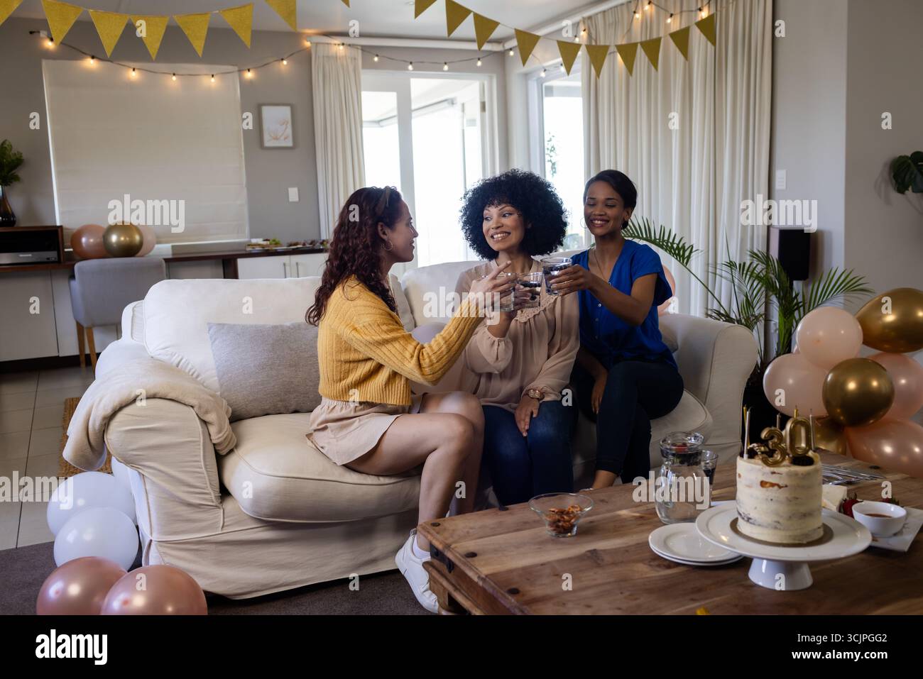 Femmes célébrant à la maison, grillant avec des boissons, entourées de décorations festives Banque D'Images