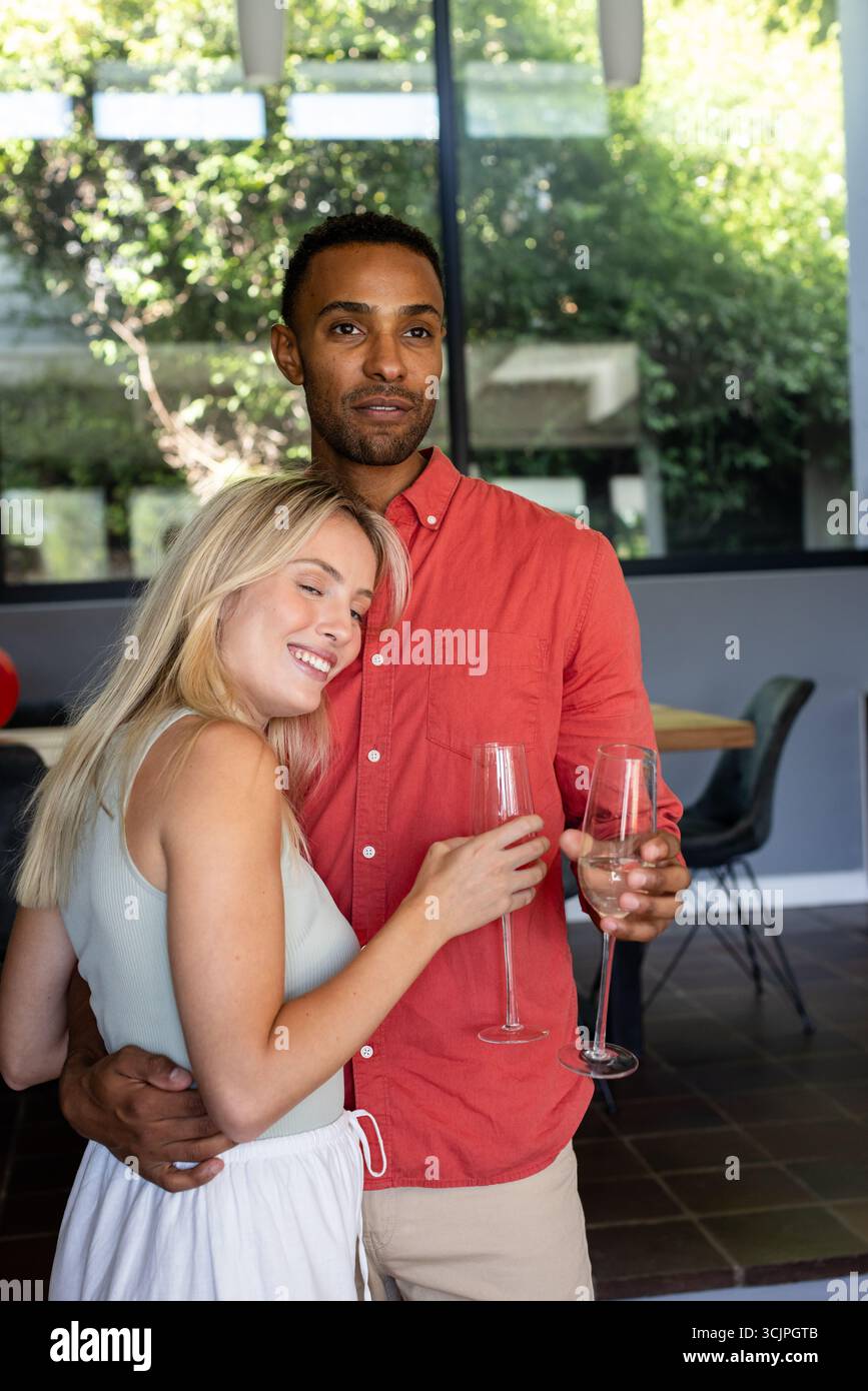 Couple célébrant à la maison, tenant des verres de champagne et souriant chaleureusement Banque D'Images