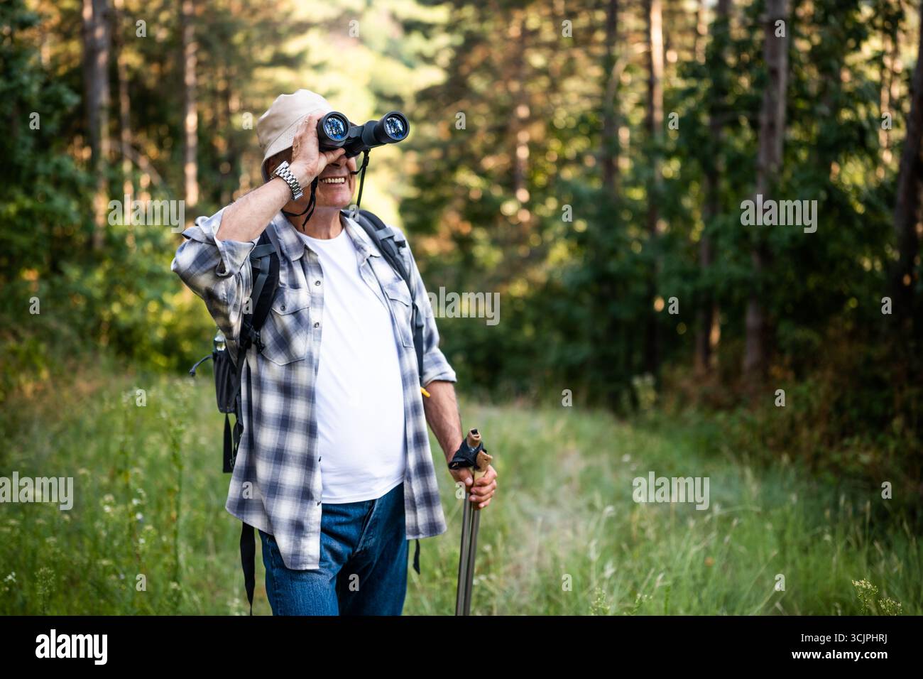 Portrait d'homme âgé avec sac à dos et bâtons de randonnée à l'aide de jumelles lors de la randonnée dans la nature. Banque D'Images