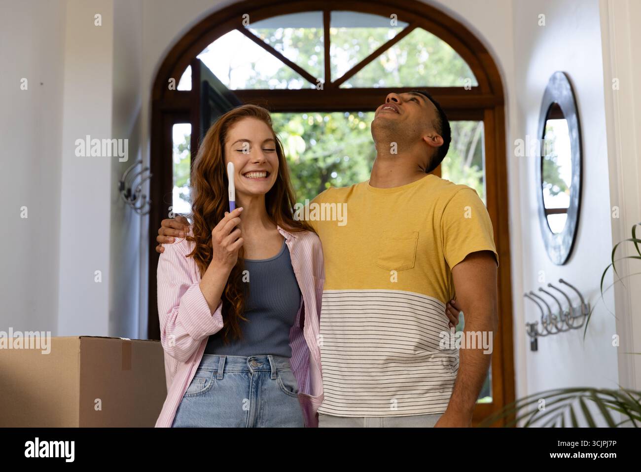 Jeune couple célébrant un résultat positif de test de grossesse à la maison, embrassant joyeusement Banque D'Images