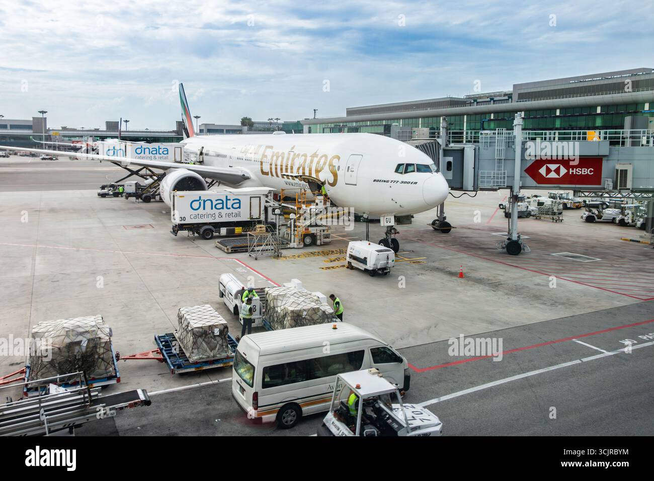 Un Boeing 777 Emirates en cours d'entretien à la porte d'embarquement de l'aéroport de Changi singapour avec du personnel au sol et de l'équipement en action par temps clair Banque D'Images