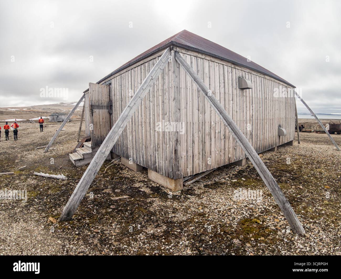 Station Kinnvika Nordaustlandet Svalbard Norvège // NORDEAUSTLANDET, Svalbard — la station Kinnvika, avant-poste de recherche historique, est située sur Nordaustlandet, la deuxième plus grande île de l'archipel du Svalbard en Norvège. Cette structure en bois, avec sa façade altérée et son contreventement extérieur proéminent, reflète l'architecture utilitaire souvent trouvée dans les environnements de recherche polaire. Le paysage environnant est caractérisé par un terrain rocheux et clairsemé, typique du Haut-Arctique. Au loin, d'autres structures et équipements abandonnés font allusion à l'utilisation passée du site comme base scientifique Banque D'Images