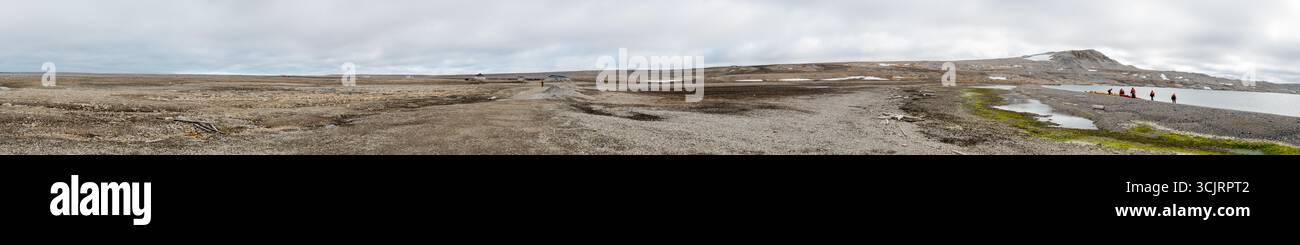 Station Kinnvika Panorama Nordaustlandet Svalbard Norvège // NORDEAUSTLANDET, Svalbard et Jan Mayen — Un panorama haute résolution capture l'avant-poste de recherche éloigné de la station Kinnvika sur Nordaustlandet, Svalbard. La station est située dans un paysage arctique sans arbres caractérisé par la toundra, les rives de gravier et une étendue d'eau calme. Plusieurs petits bâtiments, certains semblant altérés, sont visibles au loin, suggérant l'utilisation historique et continue de la station pour la recherche scientifique dans cet environnement extrême. Au premier plan, sur le rivage rocheux, bateaux gonflables et kayaks a Banque D'Images