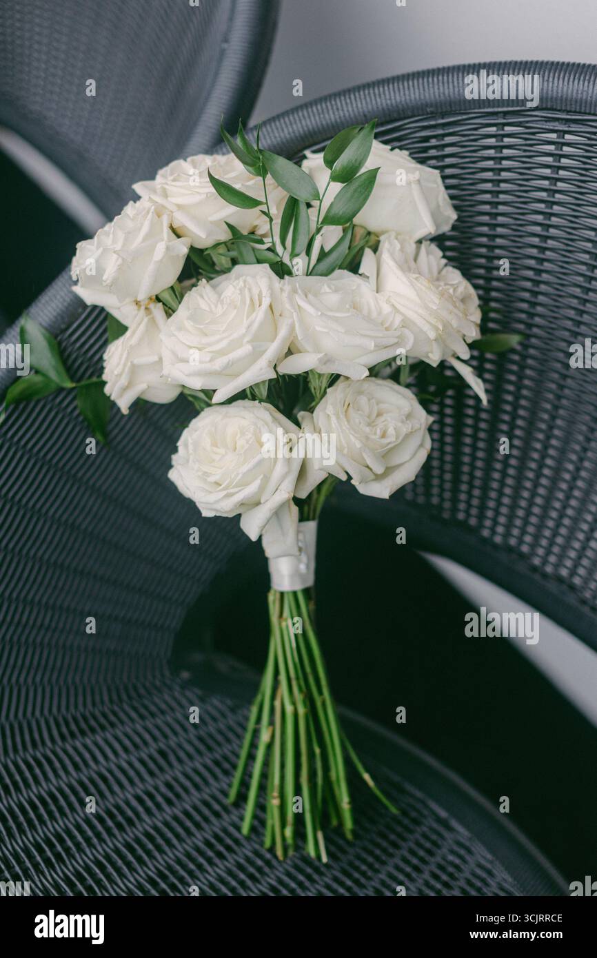 Des roses blanches attachées ensemble avec des feuilles vertes reposent gracieusement sur une chaise, mettant en valeur une touche d'élégance et de simplicité. Banque D'Images