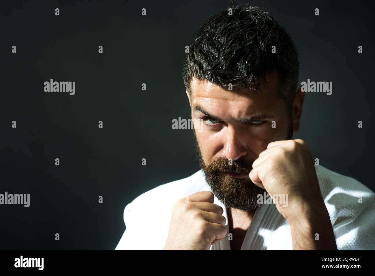 Karaté homme en posture de combat. Le combattant masculin de karaté pratique des coups de poing pendant l'entraînement de karaté. Homme barbu en kimono avec les mains serrées dans le poing prêt t Banque D'Images