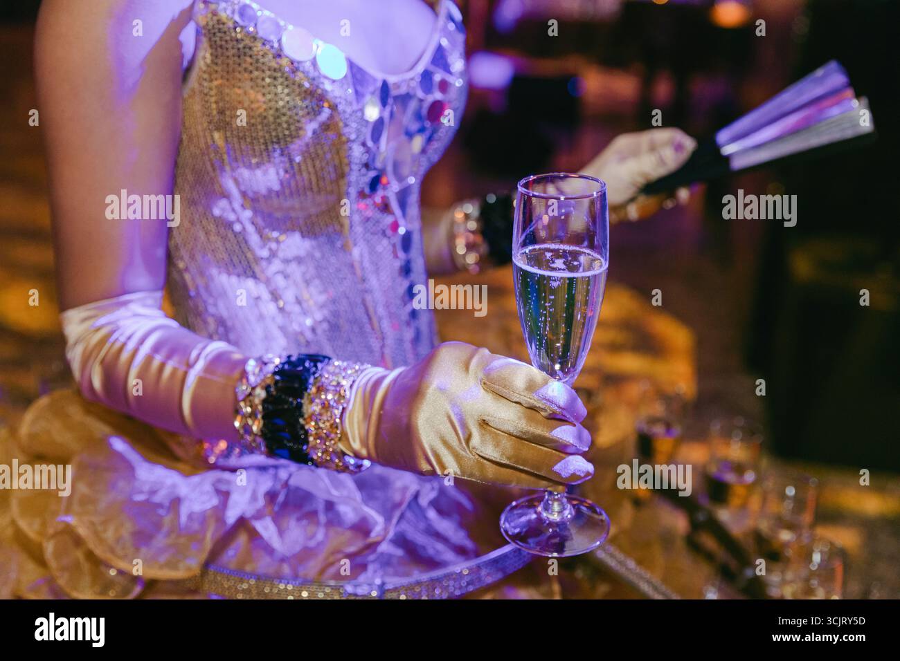 L'interprète en costume élégant tient une flûte à champagne tout en divertissant les invités lors d'une réunion de soirée haut de gamme. Banque D'Images