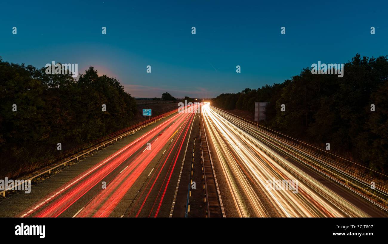 Photographie longue exposition de voitures conduisant sur une autoroute au crépuscule, créant des traînées de lumière avec la lune en arrière-plan Banque D'Images