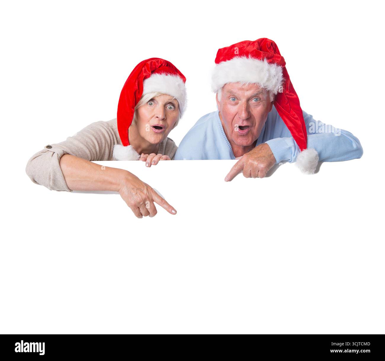 Couple senior dans les chapeaux de Père Noël pointe à une affiche blanche Banque D'Images
