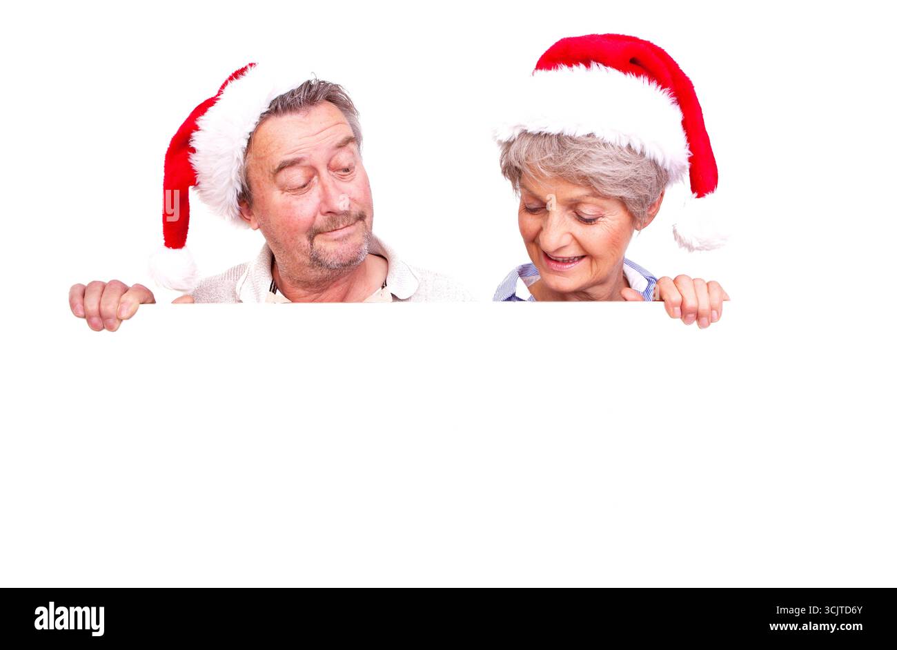 Deux aînés avec des chapeaux de Père Noël regardant une affiche blanche vierge, vue de face Banque D'Images