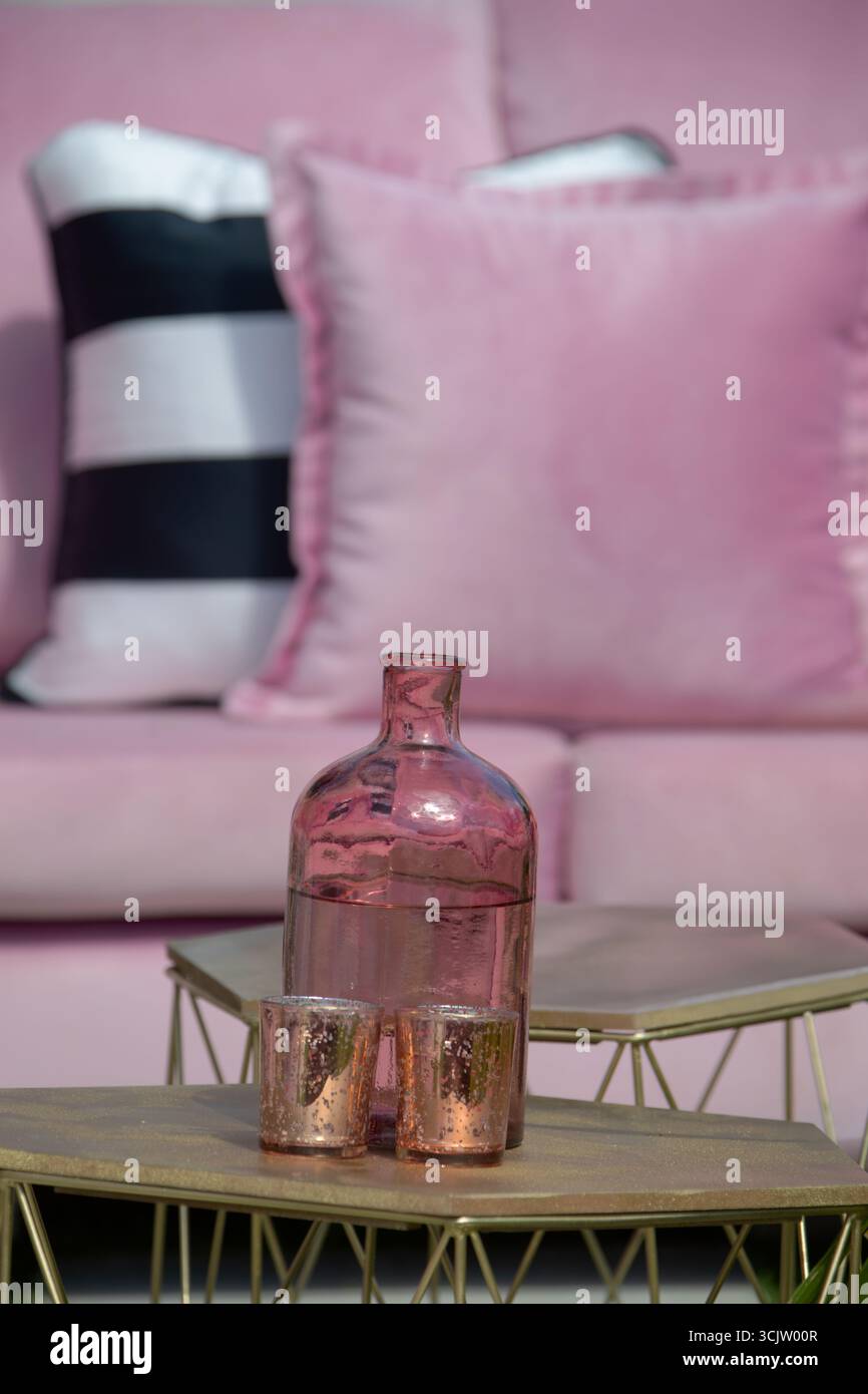 tables décoratives, grande bouteille de vase en forme de bouton clair avec deux verres, couleurs pastel canapé rose avec oreillers, table dorée mobilier de jardin à l'extérieur Banque D'Images
