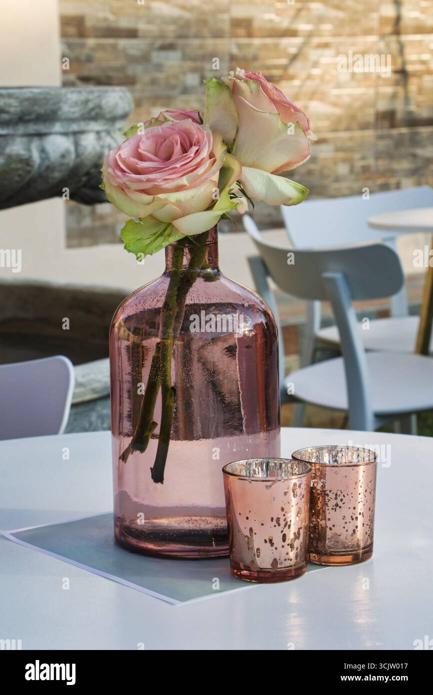 tables de décoration, grande bouteille de vase de bourgeons clair avec deux verres, couleurs pastel rose, table et chaises, meubles de jardin à l'extérieur Banque D'Images