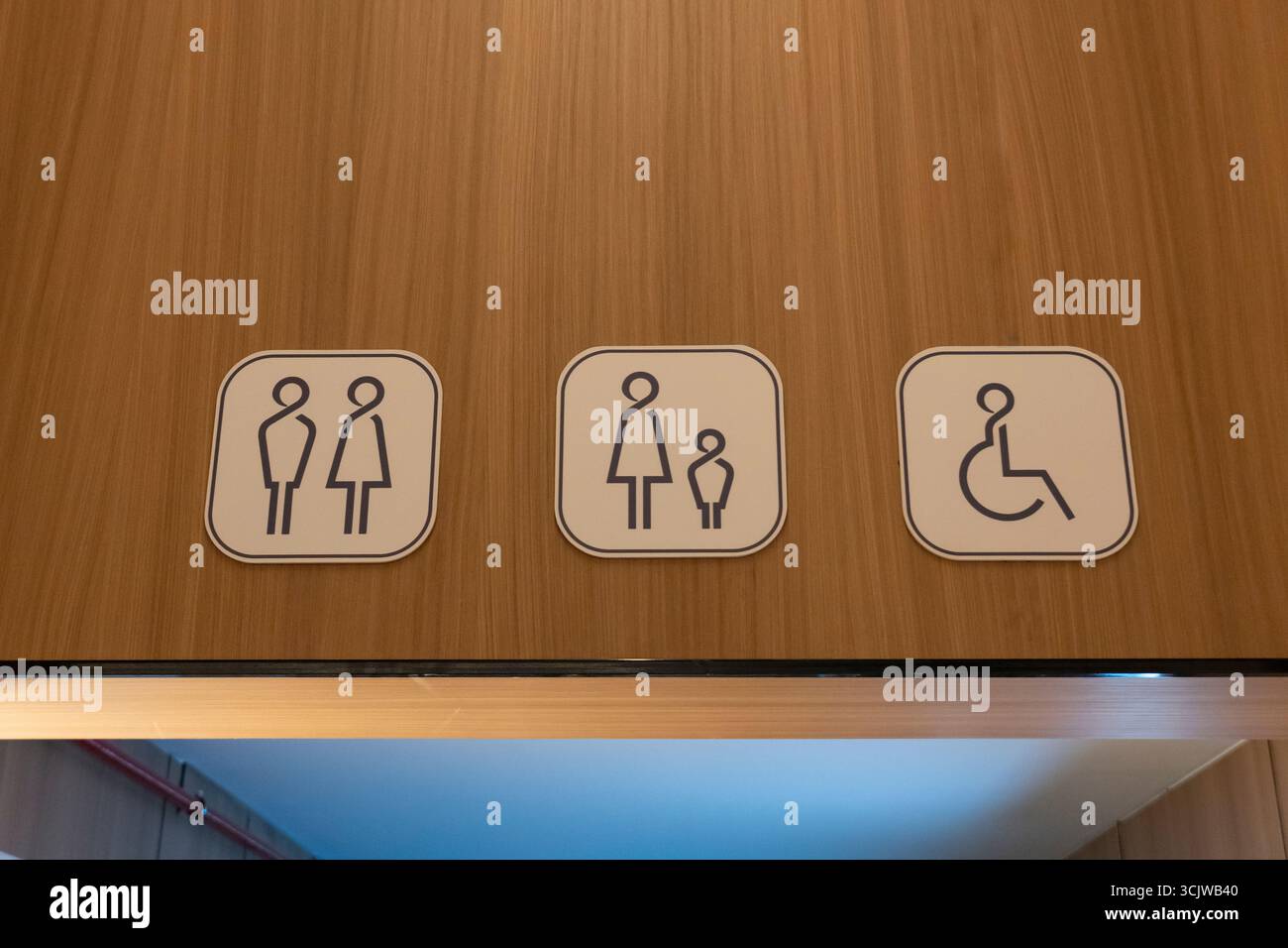 Toilettes carrées et panneaux d'accessibilité avec icônes bleues sur fond blanc, montés sur un mur en bois, indiquant unisexe, familial et fauteuil roulant-acc Banque D'Images