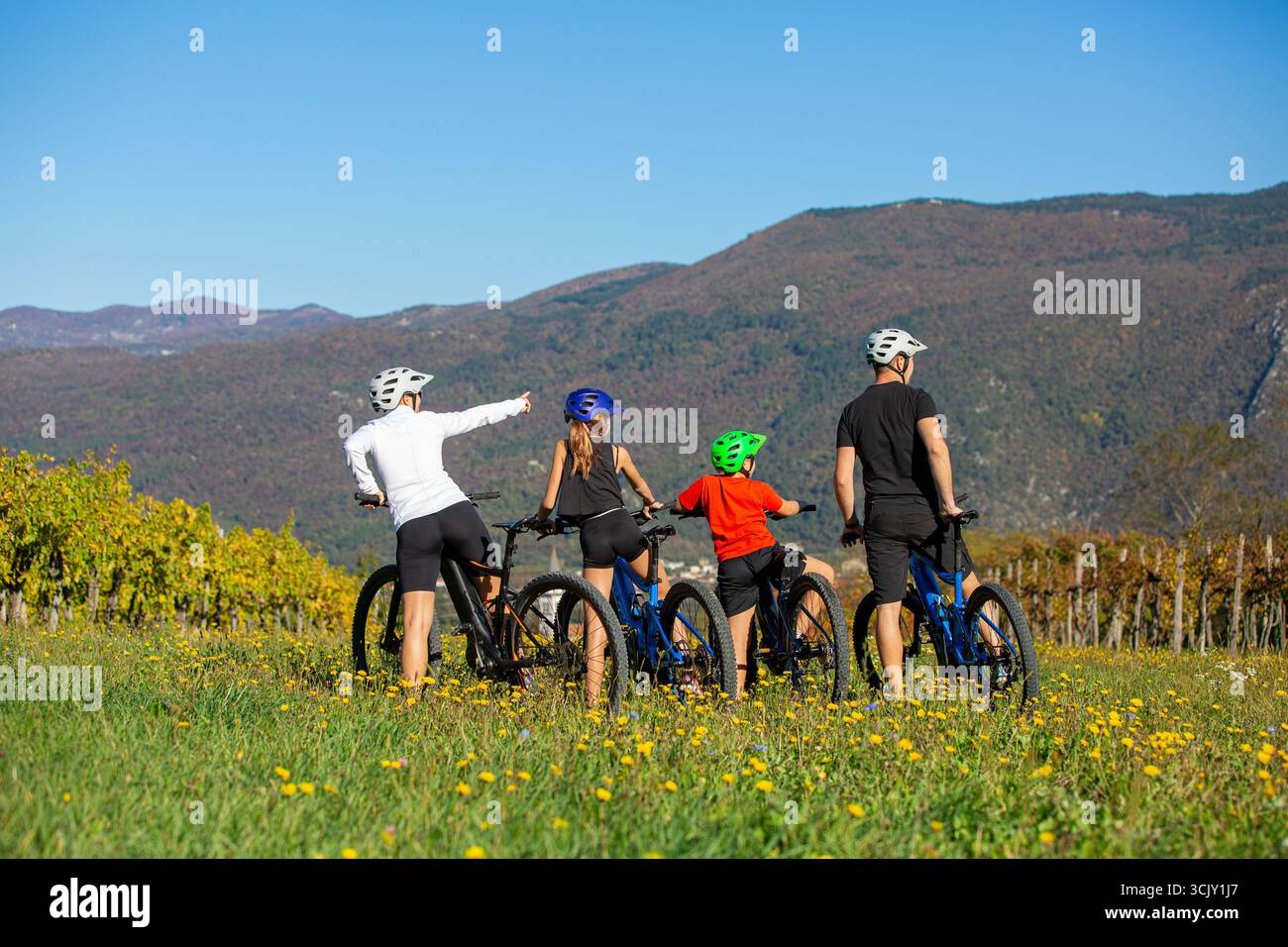 Les parents et les enfants font une pause pendant leur balade en vélo électrique, en profitant de la vue sur les vignobles et les paysages de montagne par une journée ensoleillée en plein air. Banque D'Images