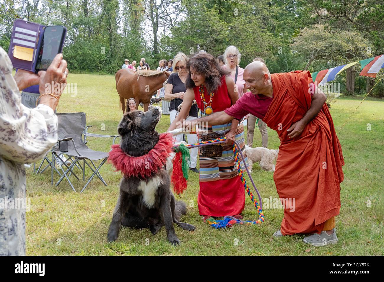 Lors d'un festival de bénédiction des animaux bouddhistes tibétains à Redding CT, un moine bénit un grand chien Mastiff tibétain tandis que son propriétaire habillé de couleurs vives le regarde. Banque D'Images