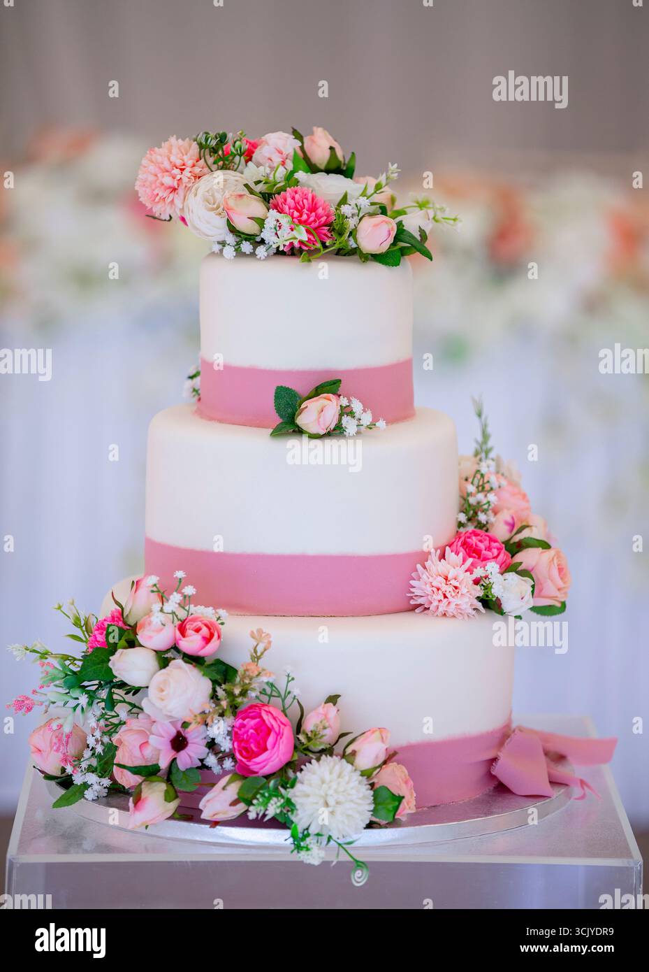Élégant gâteau de mariage à trois niveaux orné de délicates fleurs roses et blanches, orné d'un ruban rose doux Banque D'Images
