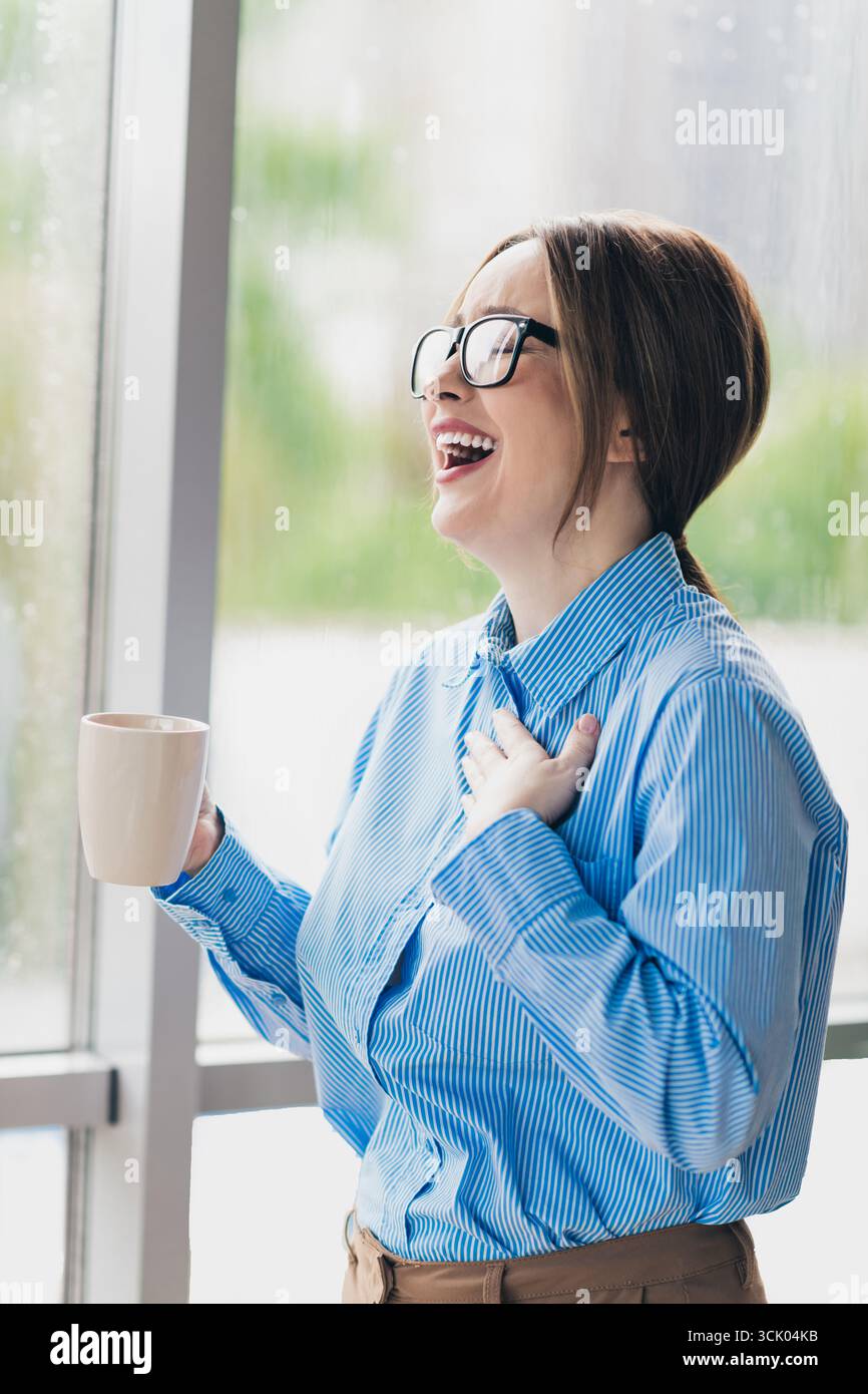 Jeune femme d'affaires riant avec une tasse à café dans un cadre de bureau moderne lumineux profitant d'un moment joyeux Banque D'Images