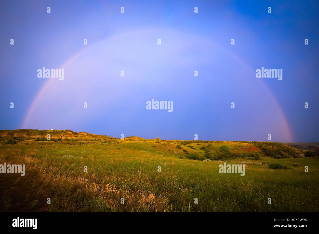 Une image à couper le souffle capture les couleurs vives d'un magnifique coucher de soleil peignant le ciel, avec un magnifique arc-en-ciel qui forme un arc sur de vastes prairies ouvertes Banque D'Images