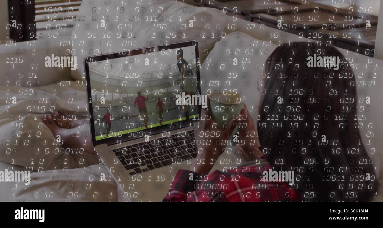 Regarder un match de football sur un ordinateur portable argenté en pyjama rouge sous superposition de code dans la chambre, espace de copie Banque D'Images