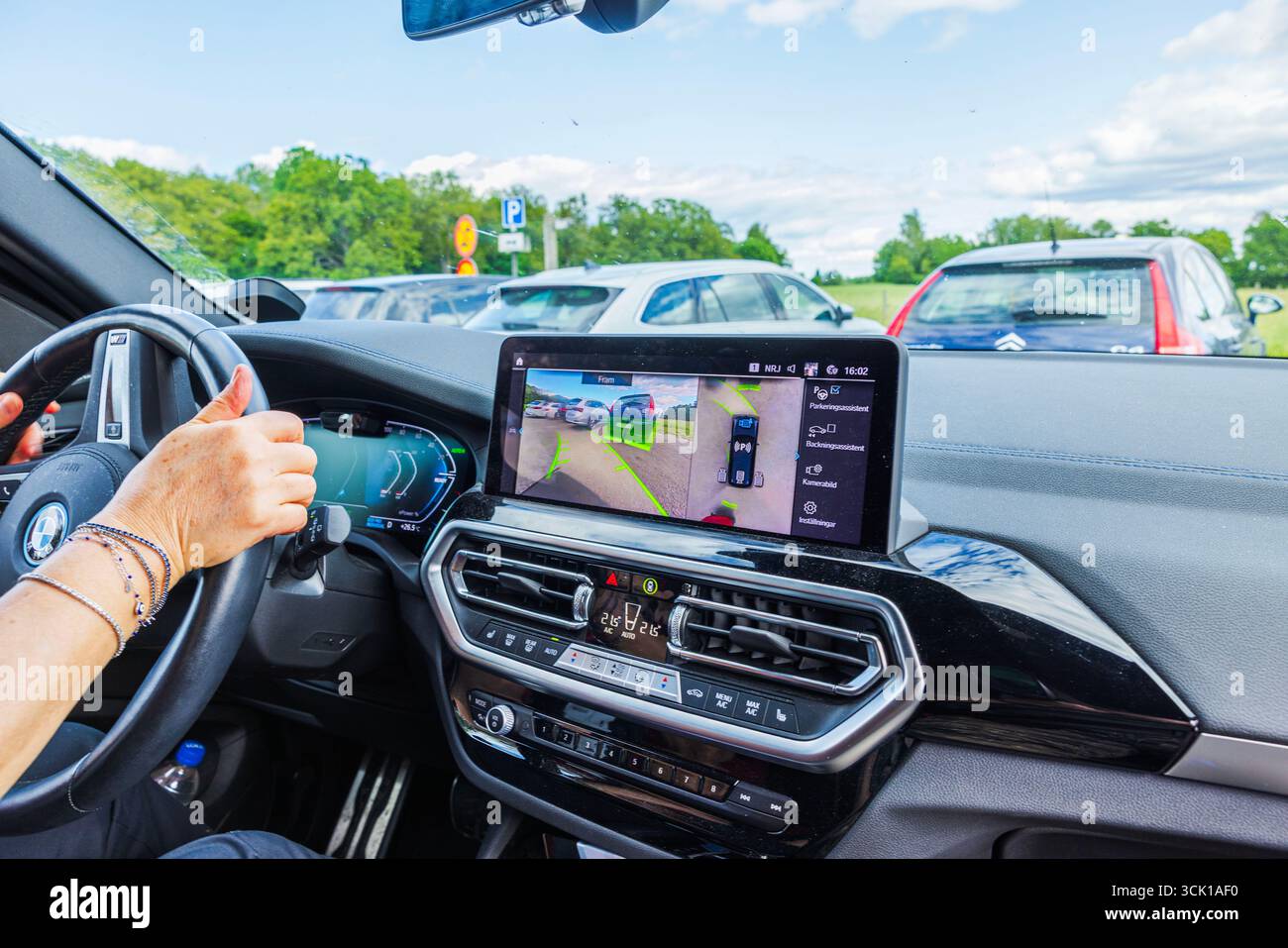 Conducteur à l'intérieur de la voiture électrique BMW iX3 M utilisant l'assistant de stationnement avec affichage de la caméra de recul sur l'écran. Suède. Banque D'Images