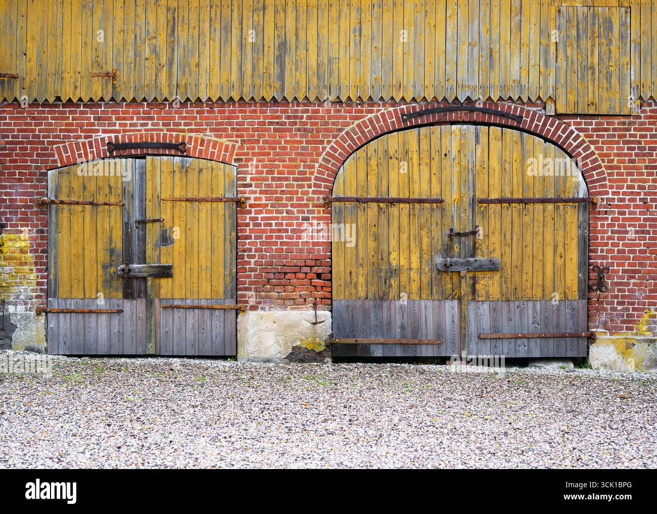 Deux grandes portes de grange rustiques, en bois jaune altéré encadrées par des arches en briques rouges, se tiennent côte à côte. Banque D'Images