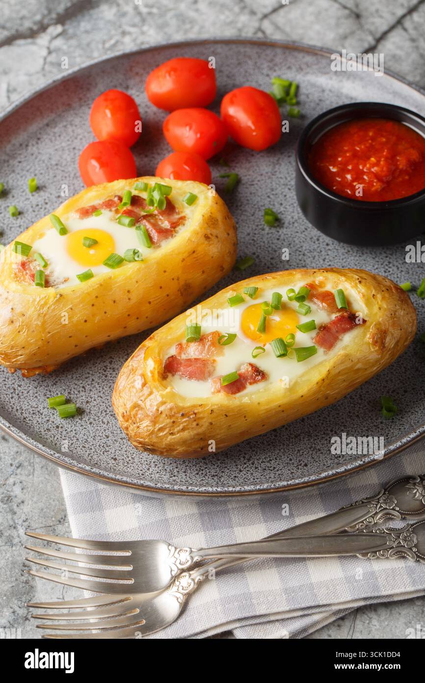 Petit déjeuner pommes de terre cuites au four avec bacon et oeuf gros plan sur l'assiette sur la table. Vertical Banque D'Images