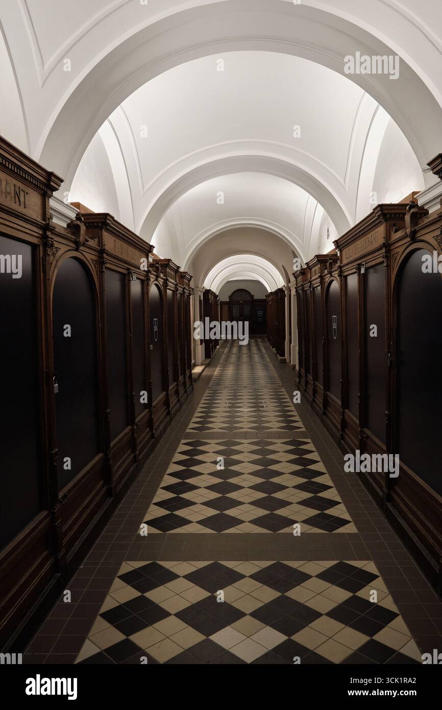 Couloir voûté dans un bâtiment historique viennois avec étagères en bois sculpté, carrelage en diamant noir et blanc et plafond voûté blanc orné i. Banque D'Images