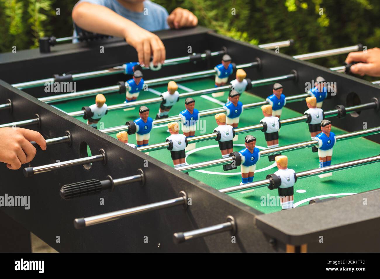 Gros plan d'un jeu de baby-foot en action avec les mains de plusieurs joueurs sur les poignées. La table présente des figurines de football en plastique classiques Banque D'Images