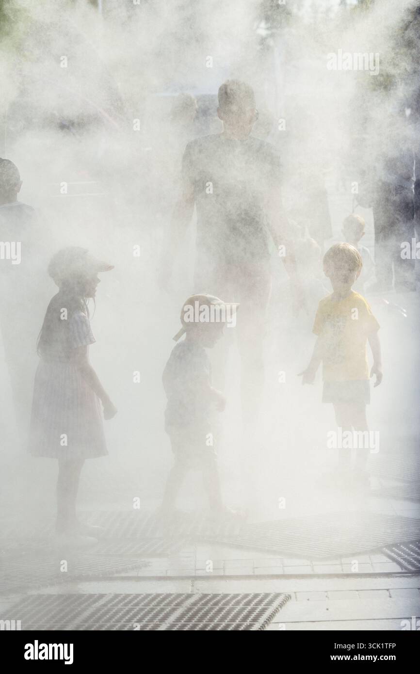 Enfants marchant dans la brume ou l'eau pulvérisée par une journée chaude. La scène capture la joie et le soulagement de se rafraîchir pendant l'été Banque D'Images