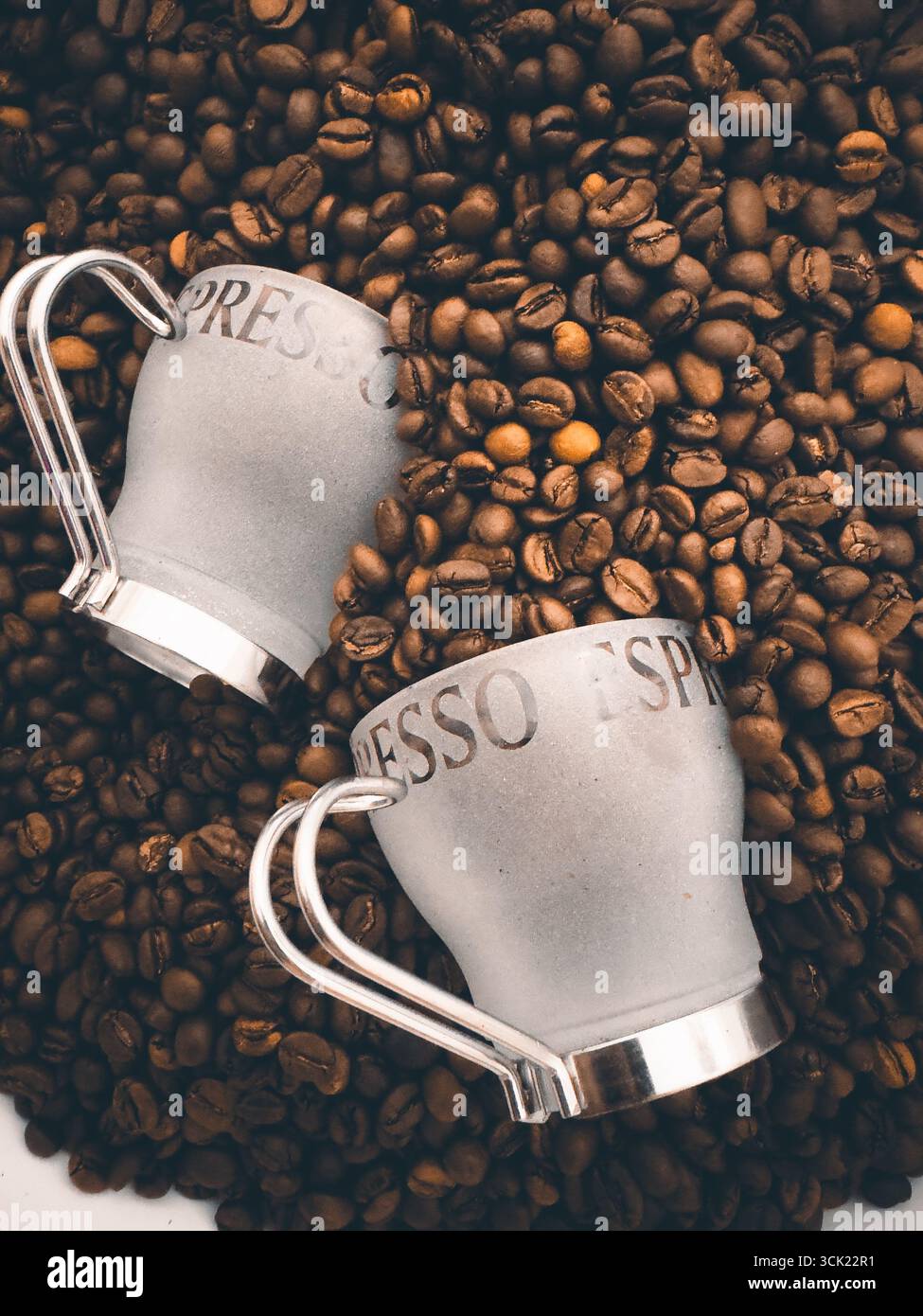 Une prise de vue à grand angle de deux tasses à espresso couchées sur un lit de grains de café torréfiés. L'image met en évidence la texture et la couleur brun foncé des haricots, whi - Image de stock capturée avec un smartphone
