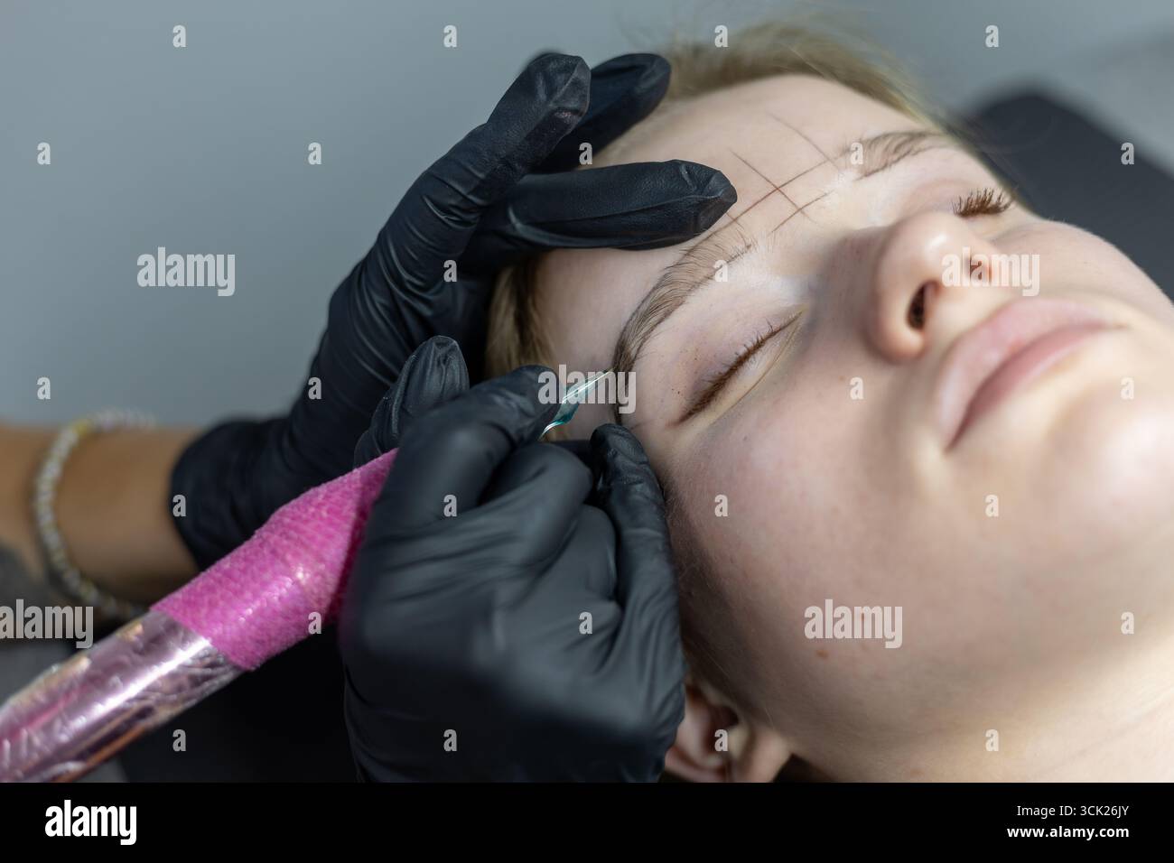 Un artiste qualifié applique soigneusement la technique de microblading pour améliorer les sourcils d'un client, en se concentrant sur des lignes précises dans un ensemble de studio de beauté moderne Banque D'Images