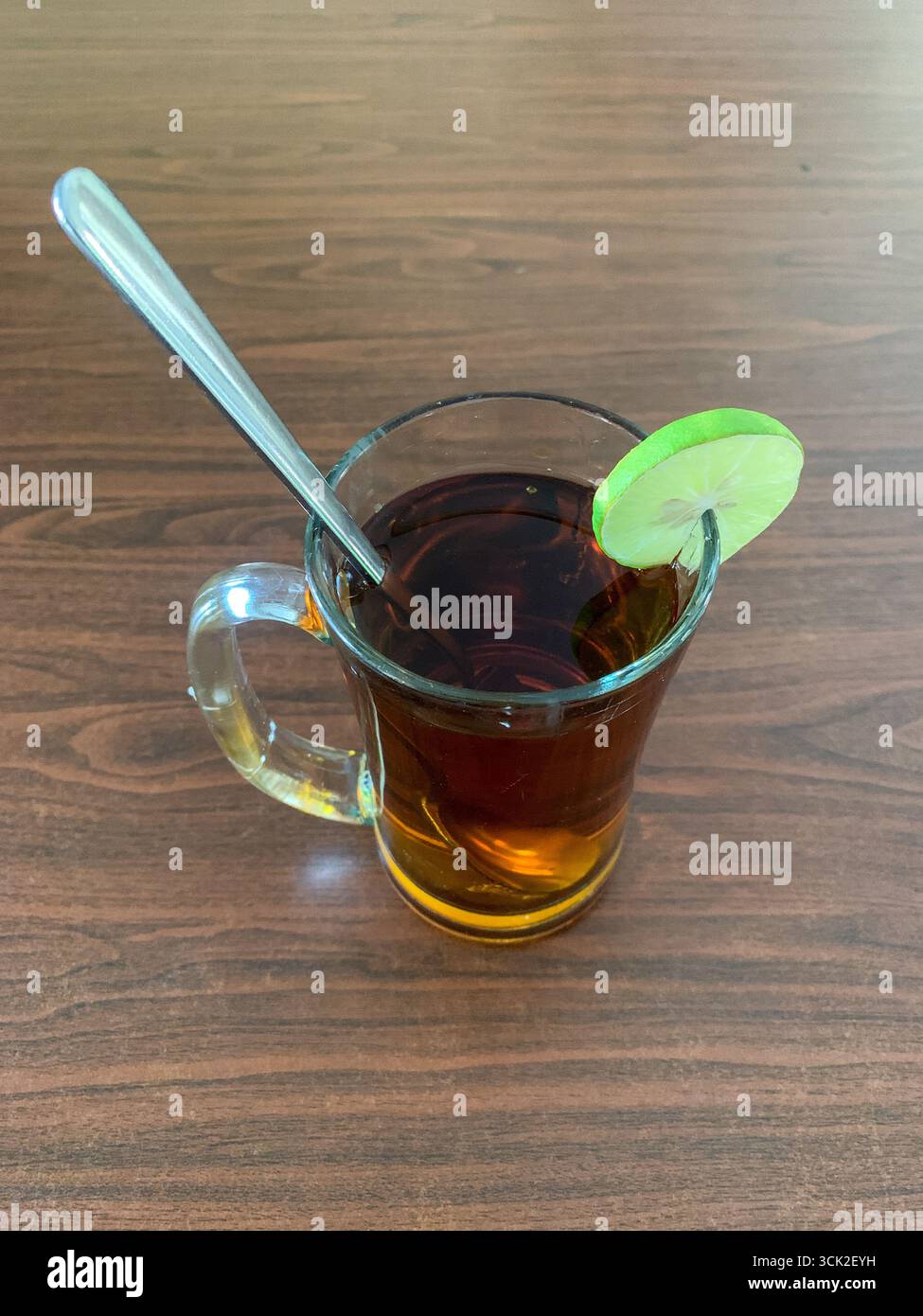 Un verre de thé noir chaud avec une tranche de citron vert sur une table en bois, boisson traditionnelle indonésienne. - Image de stock capturée avec un smartphone