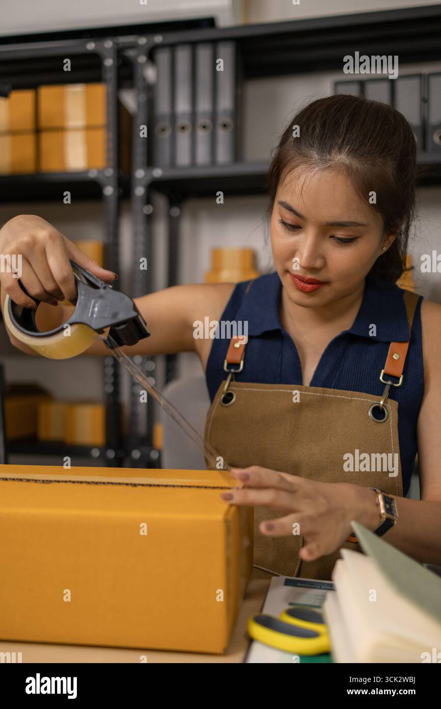 Jeune femme entrepreneure scellant soigneusement le paquet avec du ruban adhésif, préparant les commandes de marchandises, gérant l'expédition et la livraison pour son succès en ligne Banque D'Images