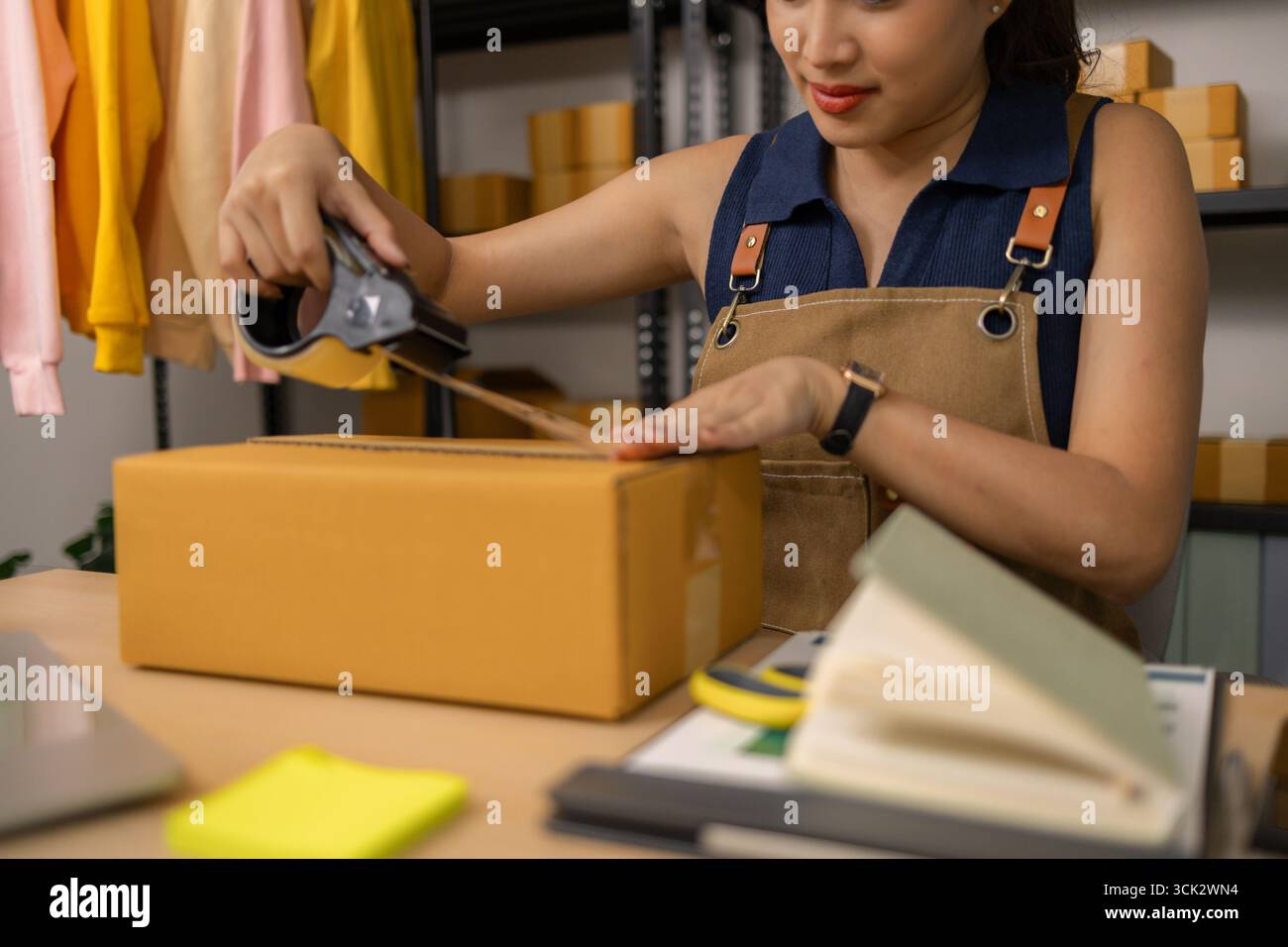 Jeune femme entrepreneure scellant soigneusement le paquet avec du ruban adhésif, préparant les commandes de marchandises, gérant l'expédition et la livraison pour son succès en ligne Banque D'Images