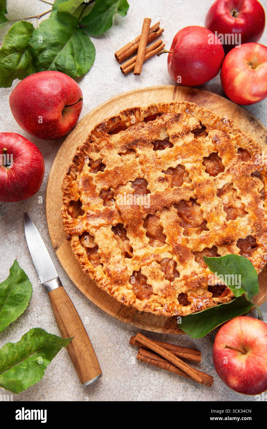 Tarte aux pommes maison entourée de pommes rouges fraîches, de bâtonnets de cannelle et de feuilles de pomme, créant une scène automnale chaleureuse et accueillante Banque D'Images