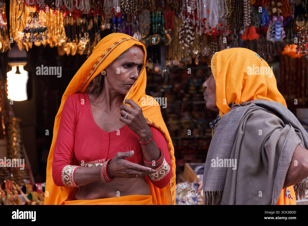 Photographie de rue de deux femmes rurales Rajasthani en robe traditionnelle parlant à l'extérieur d'un petit stand de bijoux à la Foire de Pushkar, en Inde Banque D'Images