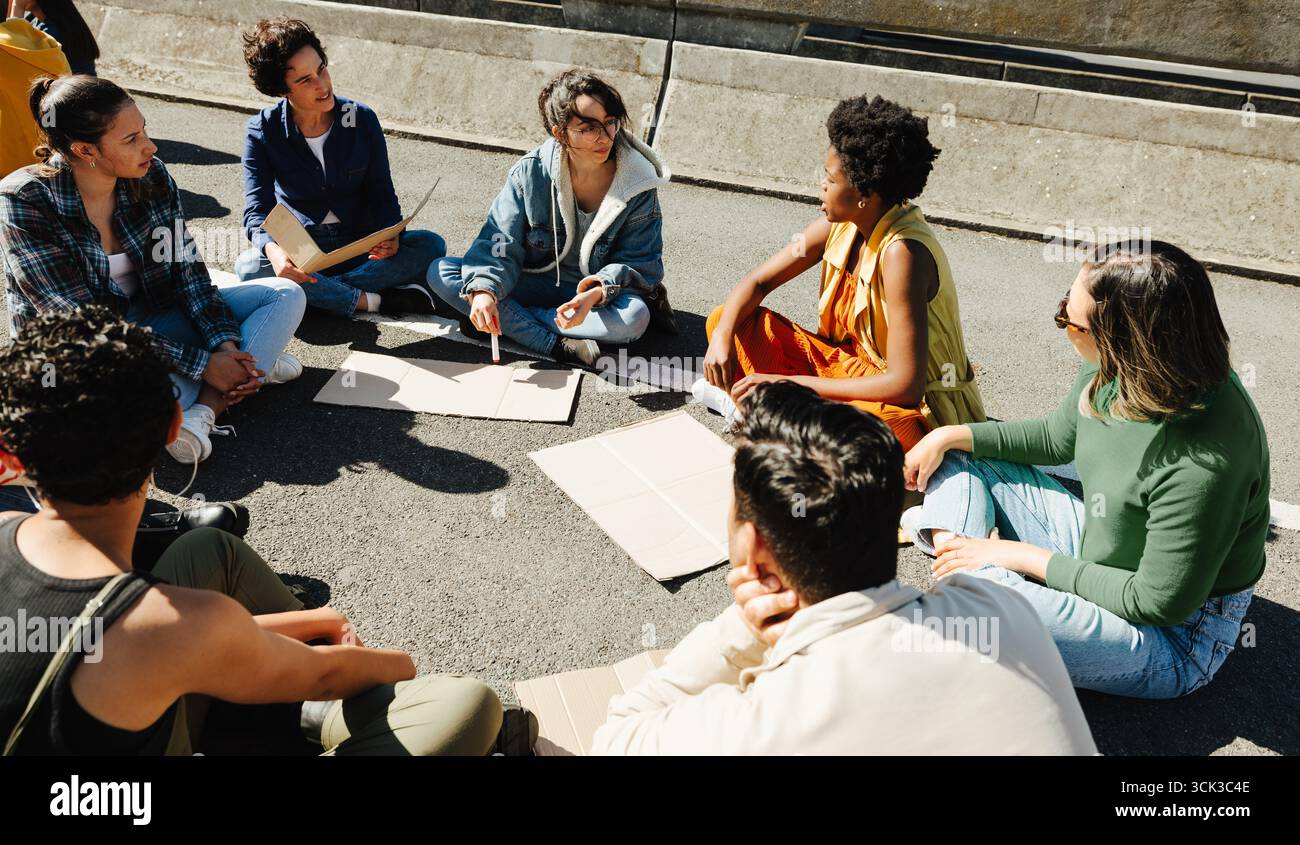Un groupe diversifié d'individus assis ensemble sur un trottoir, partageant des idées et promouvant le changement par la discussion et la planification collectives. Banque D'Images