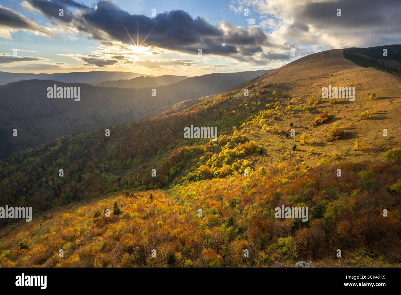 Les couleurs de l'automne enflamment les collines ondulantes tandis que le soleil éclate à travers les nuages spectaculaires sur les sereines montagnes Velka Fatra, Staré Hory, Banskobystrický kraj, Slovaquie. Banque D'Images