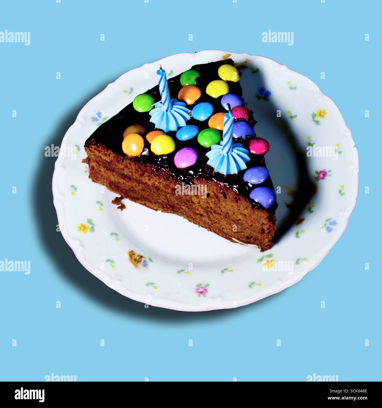 Une tranche de gâteau au chocolat décorée de bonbons colorés et de bougies d'anniversaire sur une assiette florale. Banque D'Images