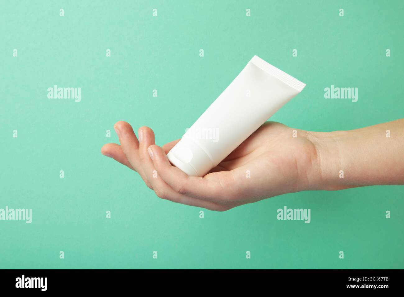 Main tenant le tube en plastique blanc blanc vierge sur fond de menthe. Maquette de marquage de produit cosmétique de beauté. Banque D'Images