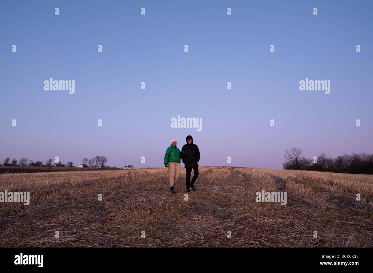 Deux individus se promènent dans un vaste champ, partageant un moment de calme alors que la nuit commence à tomber, enveloppant le paysage dans des teintes douces de crépuscule. Banque D'Images