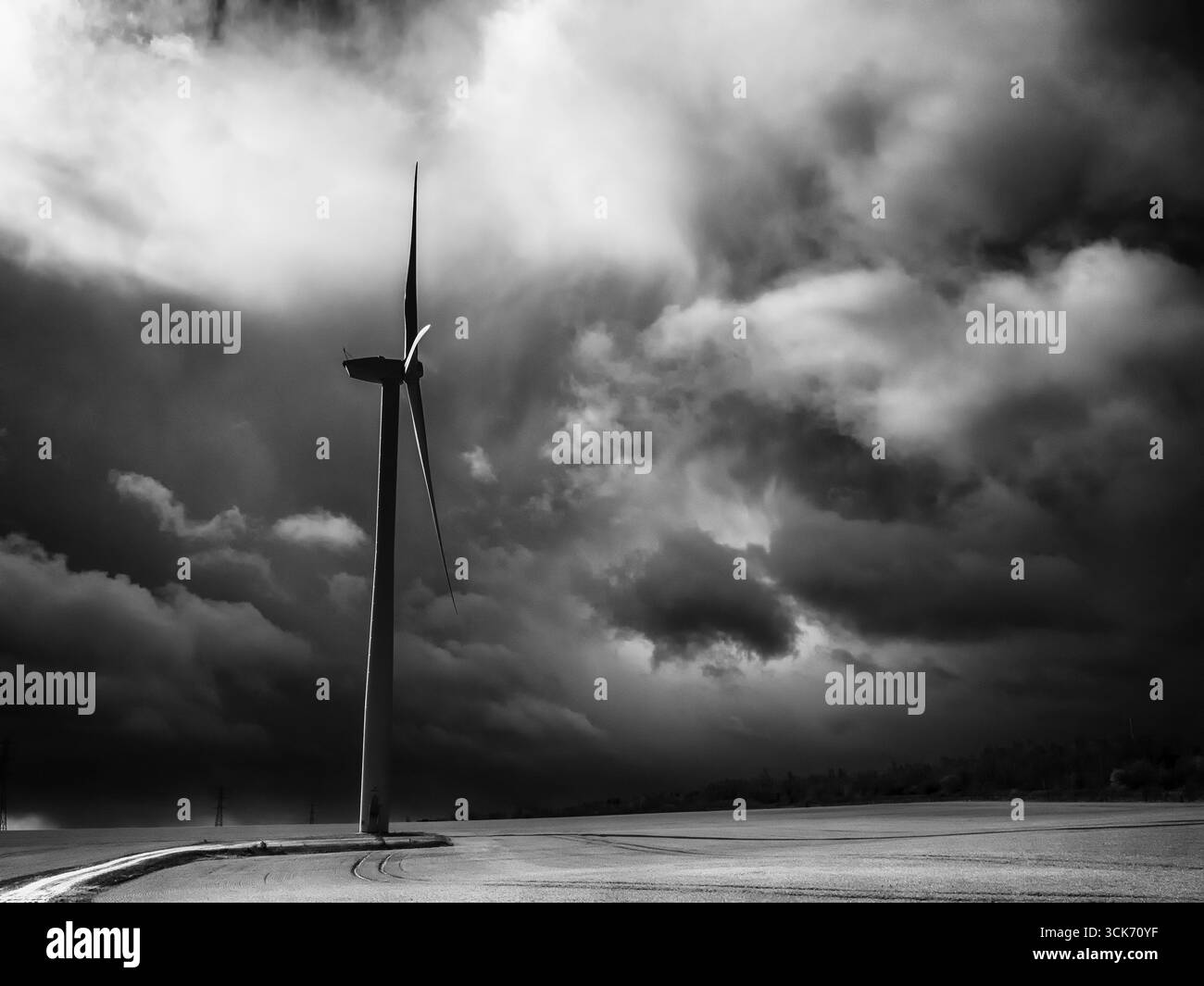 Éolienne unique debout sur des terres agricoles sous des nuages orageux spectaculaires en noir et blanc Banque D'Images