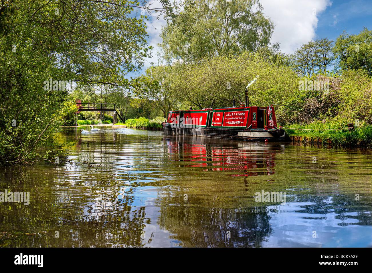 RIVER WEY bateau étroit traditionnel avec fumée de cheminée sur la rivière Wey près de High Bridge avec cygnes, amarré pour une pause le jour d'été encore au printemps Envoyer Banque D'Images