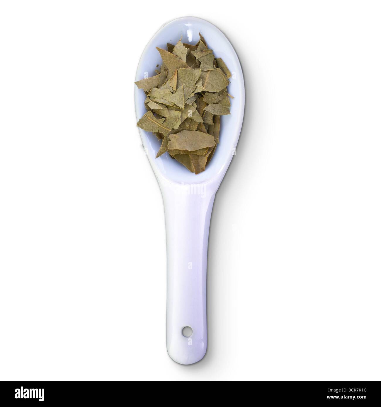 Une cuillère blanche remplie de feuilles de laurier séchées, couramment utilisée comme herbe culinaire dans divers plats. Banque D'Images